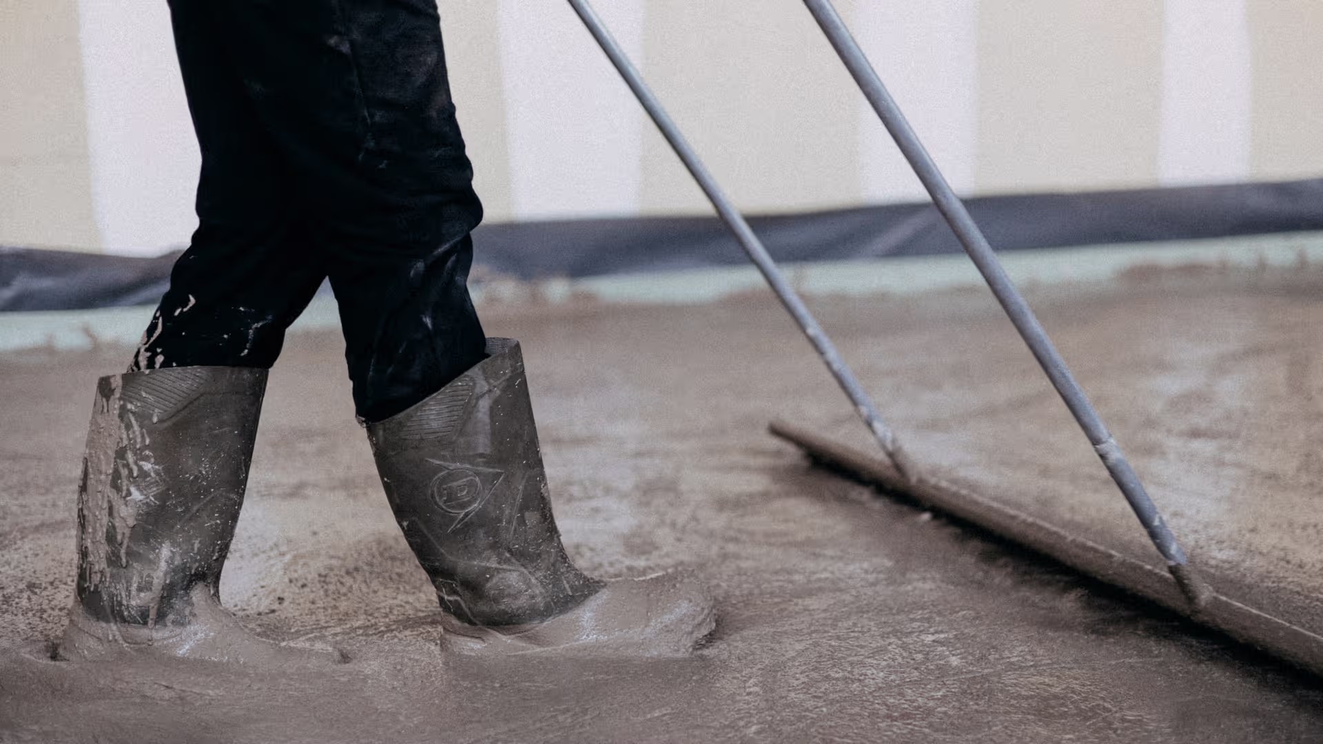 Chapiste en bottes égalisant une chape liquide fraîche à la barre de lissage