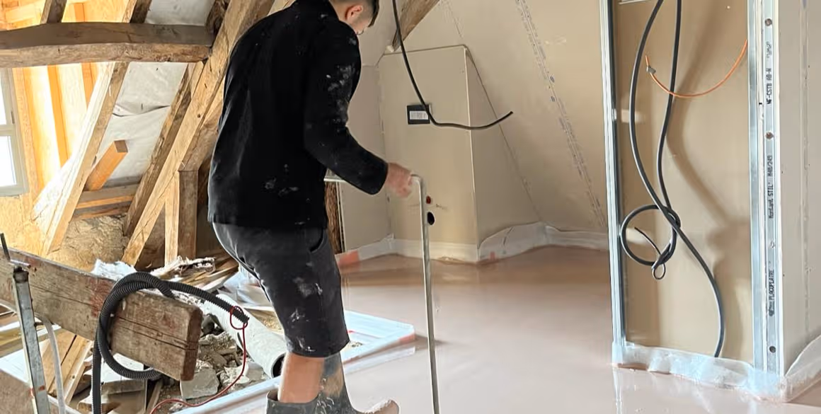 Chapiste étalant une chape fluide fraîche dans des combles en rénovation